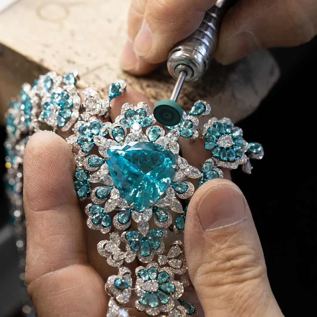 Close-up of a jeweler working on a decorative piece with blue gemstones.