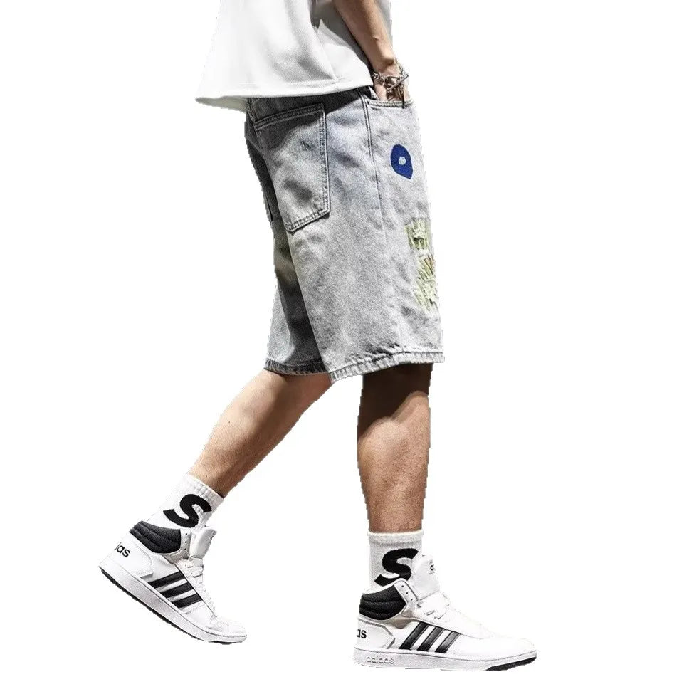 Person wearing light gray denim shorts with colorful patches and white sneakers on a white background