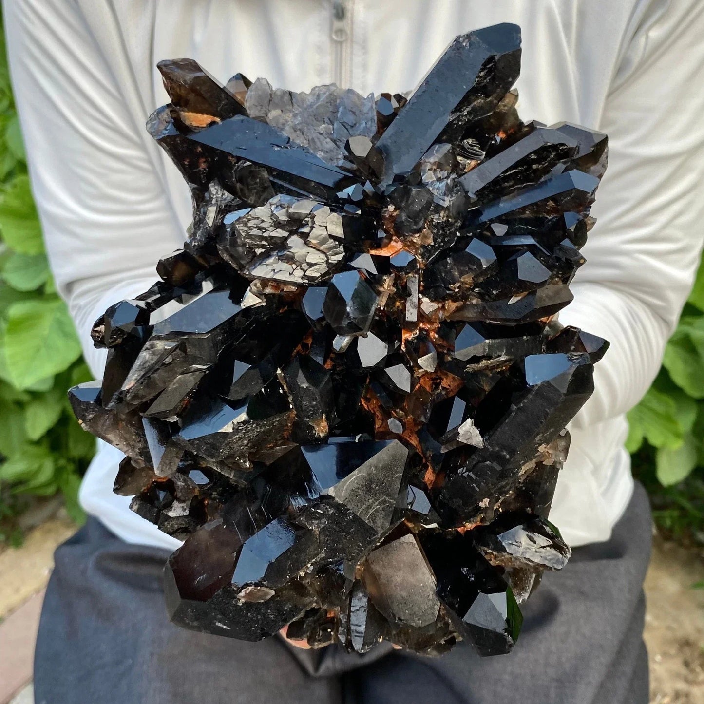 Person holding a large black crystal cluster outdoors