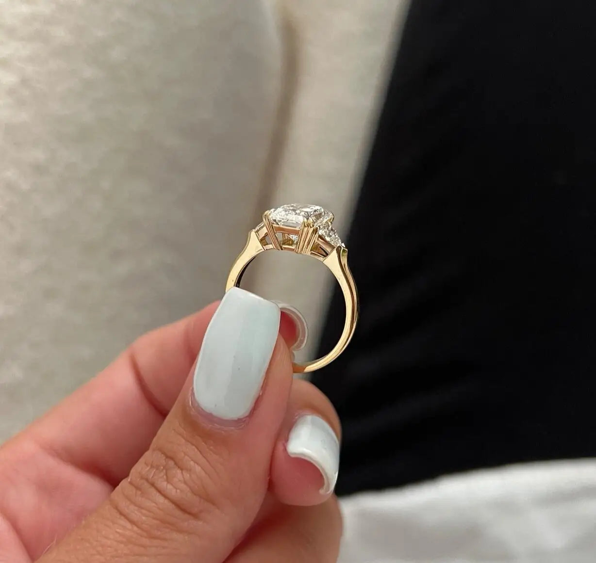 Gold ring with a diamond held by a hand with light blue nail polish.