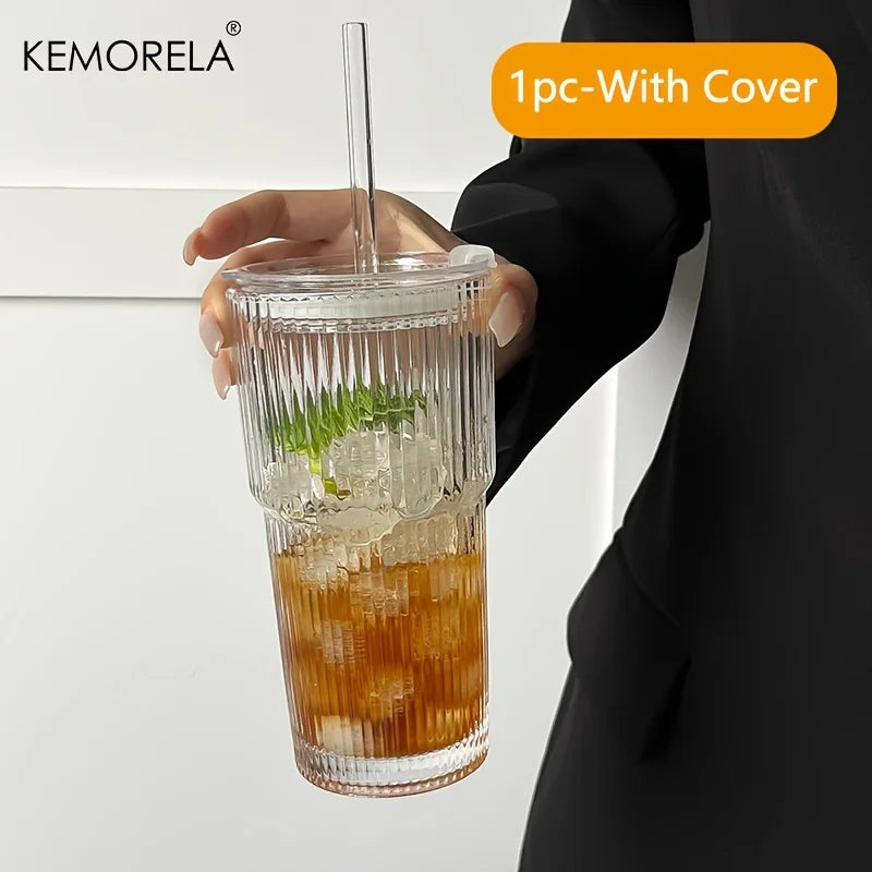 Clear glass tumbler with a cover held by a person, containing a drink with ice and a straw.