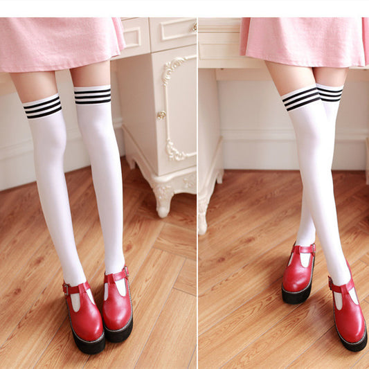White knee-high socks with black stripes worn with red shoes on a wooden floor.