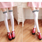White knee-high socks with black stripes worn with red shoes on a wooden floor.