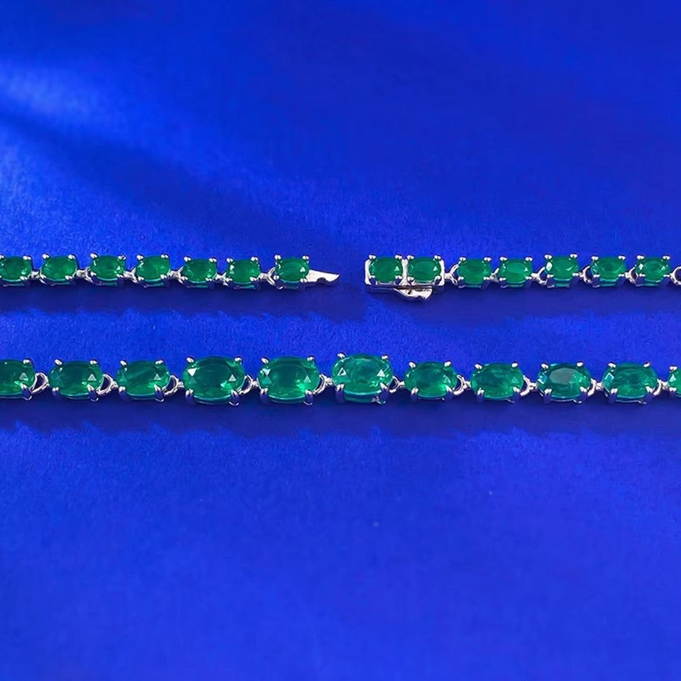 925 Sterling Silver Oval Cut Emerald Tennis Necklace laid in circle on blue velvet