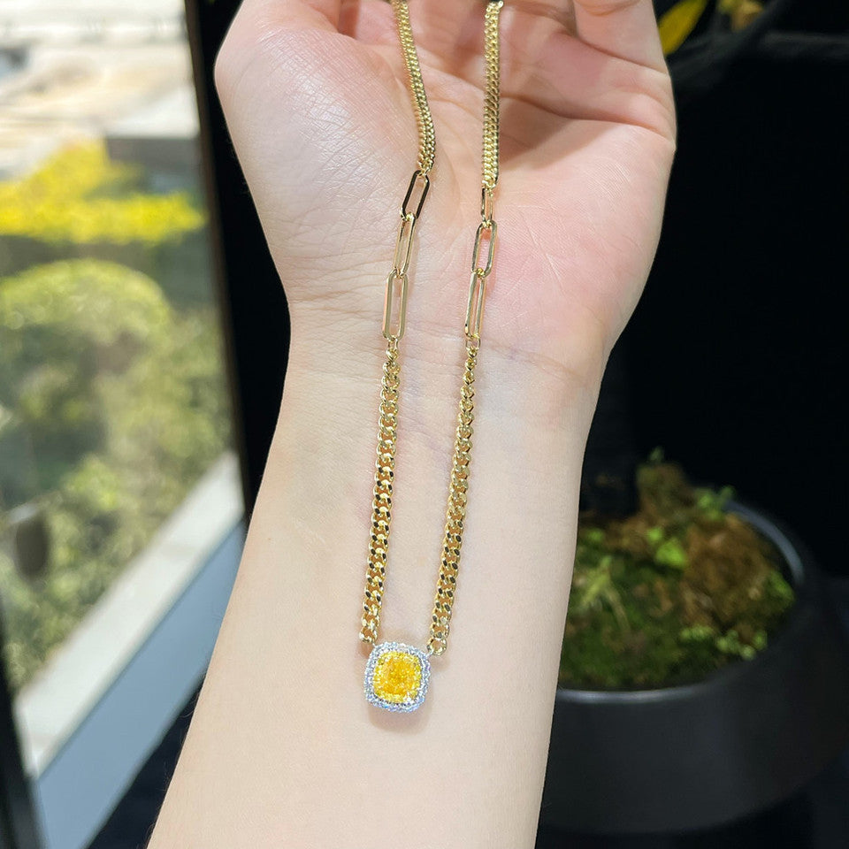 Two 18K yellow gold Cuban link necklaces with yellow diamond pendants held in hand