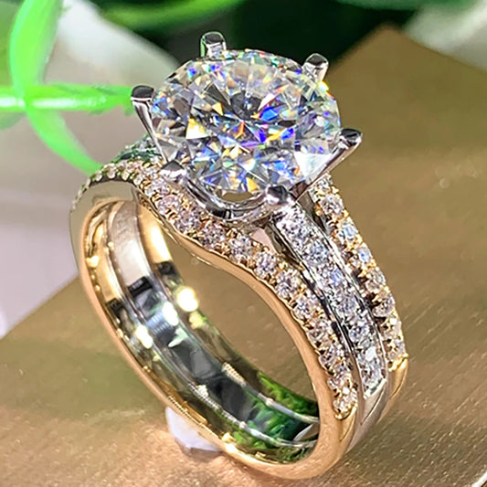 Gold and silver ring with a large diamond and smaller diamonds on the band, on a reflective surface.