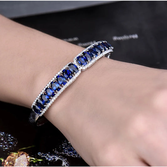 A close-up of a person's wrist wearing a silver-toned bracelet set with deep blue rectangular gemstones and small clear accent stones.