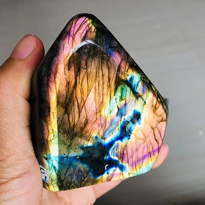 Multicolored crystal held in a hand against a neutral background