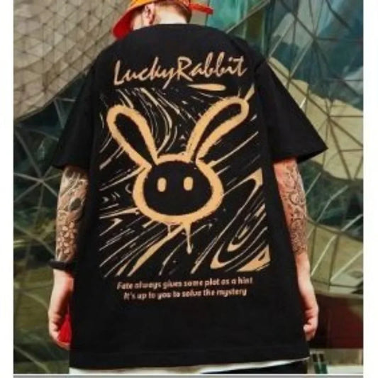 Person wearing a black t-shirt with a gold bunny logo and text, standing against a textured wall.