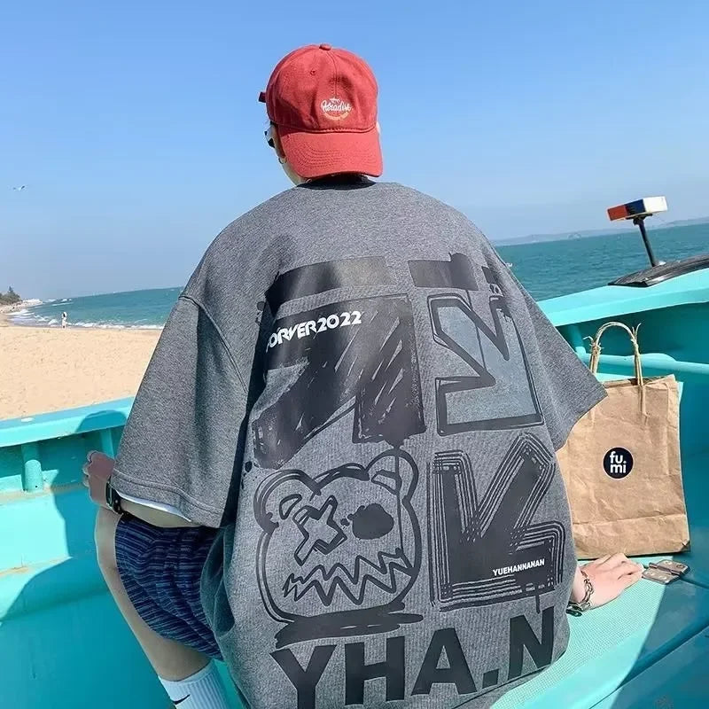 Person wearing a gray oversized t-shirt with black graphics and text, sitting on a turquoise boat.