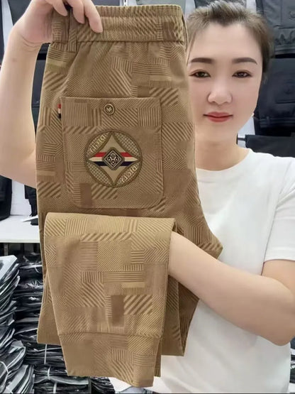 Person holding up a pair of brown pants with a brand logo, standing in an indoor setting.