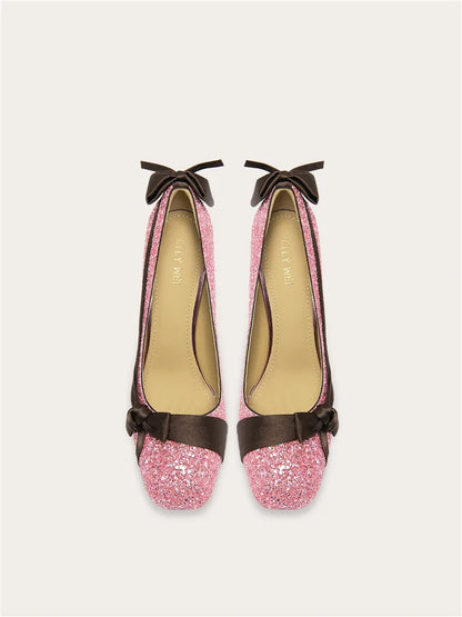 Pair of pink glittery shoes with brown bows on a white background
