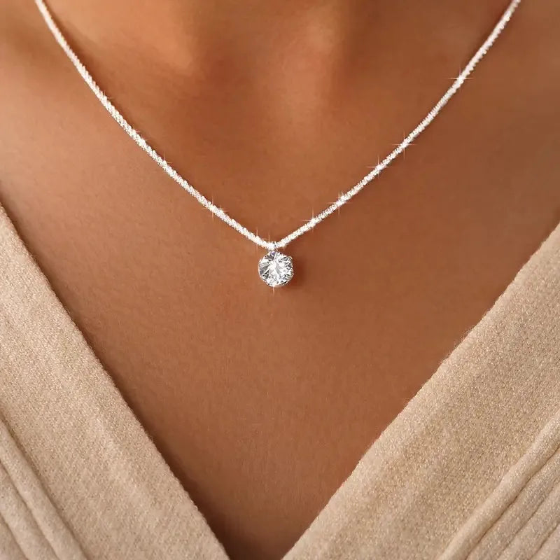 Silver necklace with a round pendant on a person wearing a beige top.