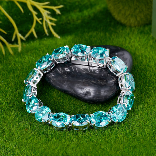 A silver-toned cuff bracelet set with large, round-cut light blue gemstones, displayed on a dark stone over a green grass-like surface.