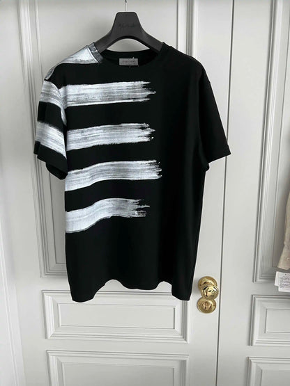 Black t-shirt with white brushstroke design on a hanger against a white door.
