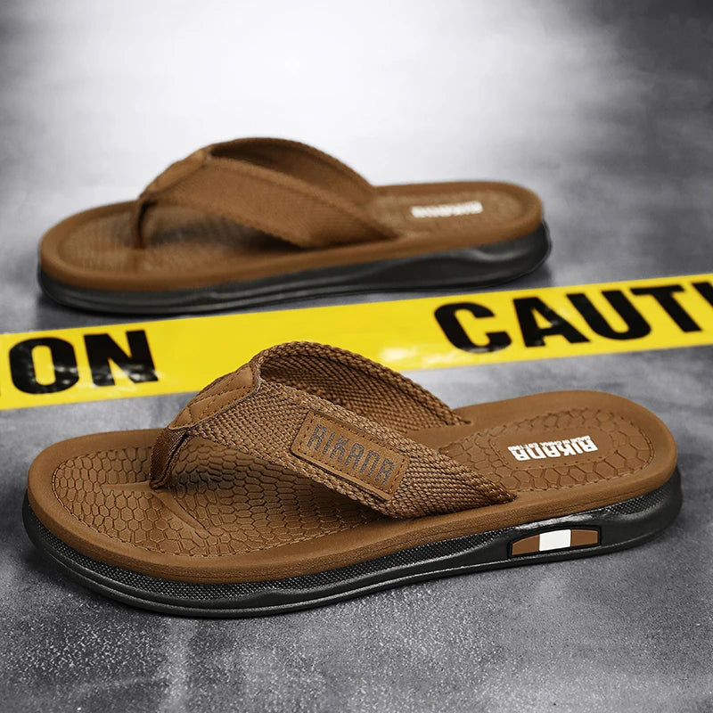 Brown sandals with a visible brand logo on a gray surface with yellow caution tape.