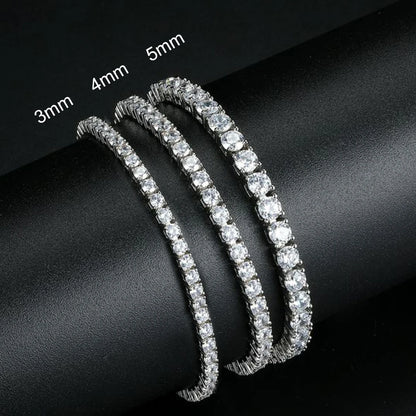 Three diamond tennis bracelets of different widths on a dark surface