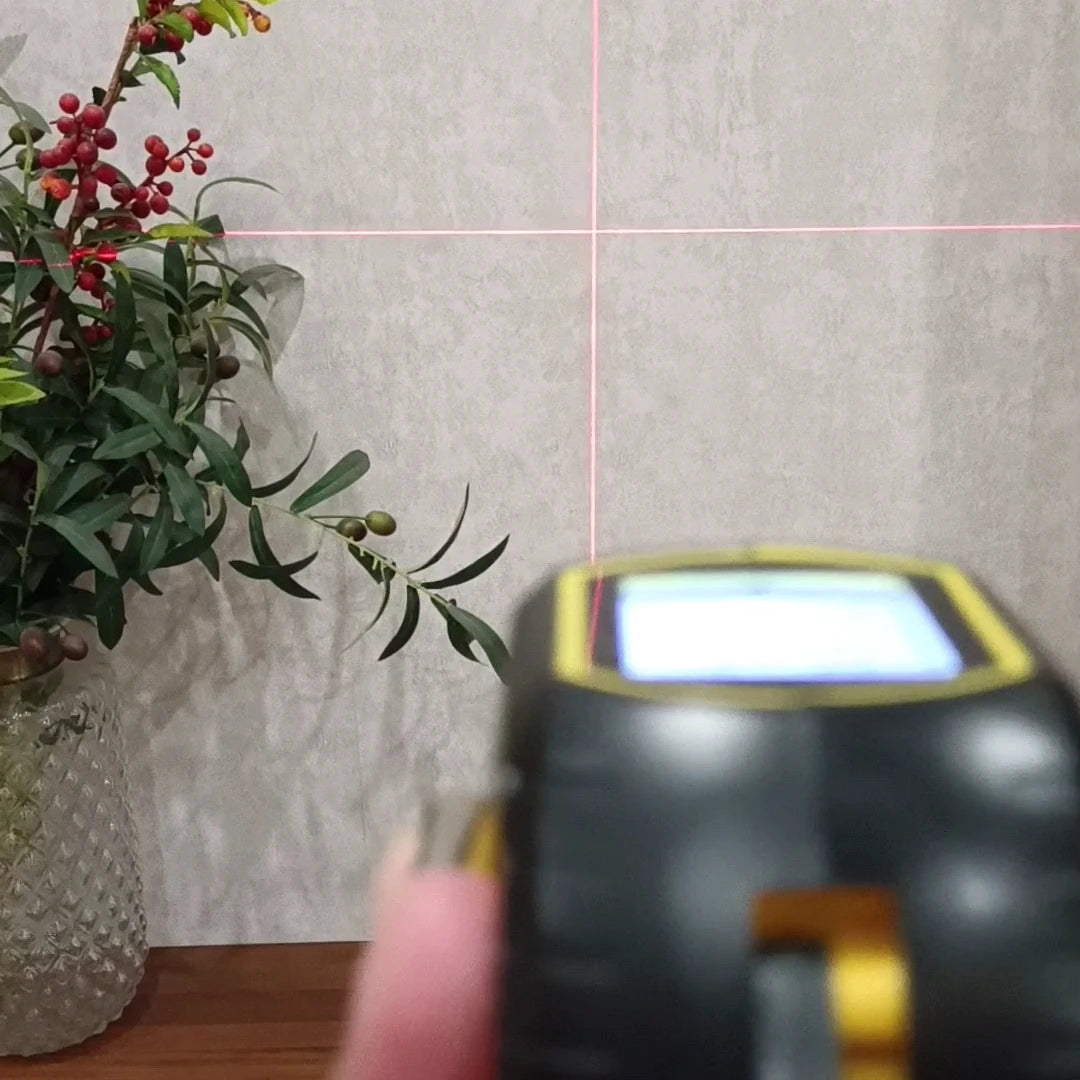 Infrared thermometer pointing at a plant against a textured wall.