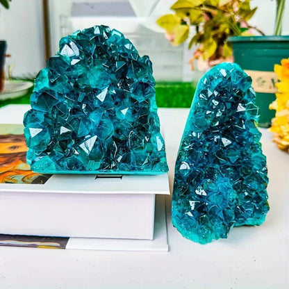 Two large turquoise crystal formations on a white surface with a blurred indoor background.