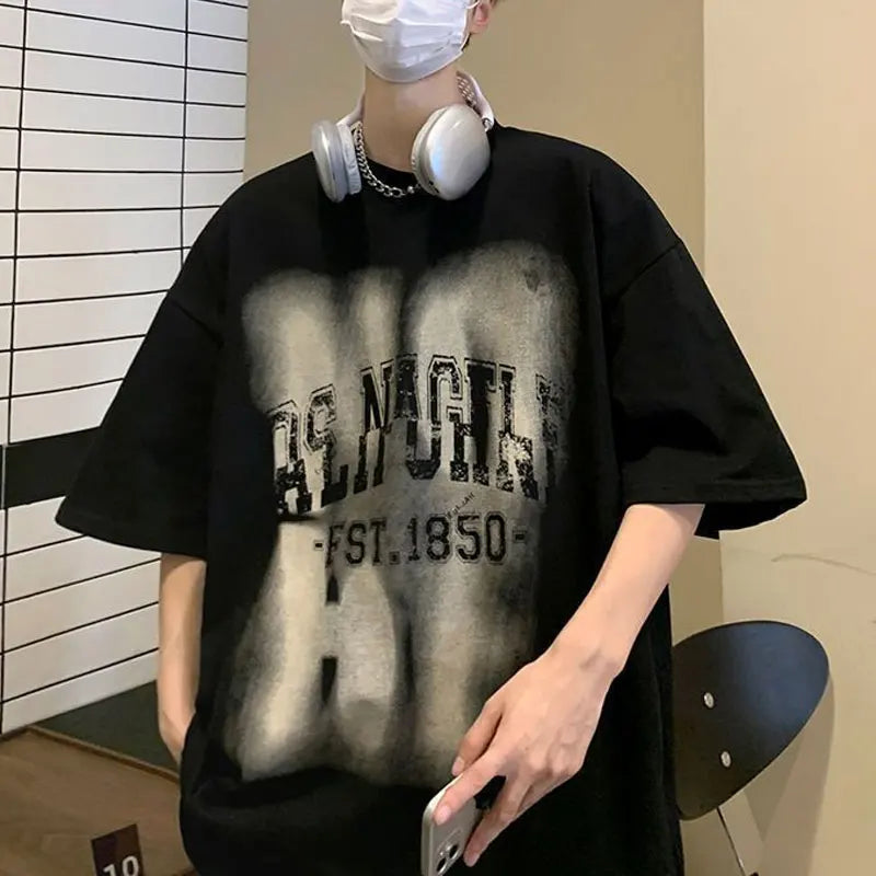 Person wearing a black oversized t-shirt with text, holding a phone, and wearing headphones indoors.