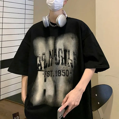 Person wearing a black oversized t-shirt with text, holding a phone, and wearing headphones indoors.