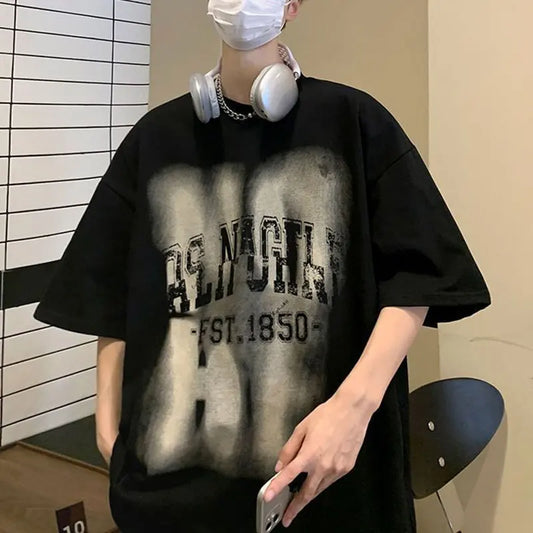 Person wearing a black oversized t-shirt with text, holding a phone, and wearing headphones indoors.