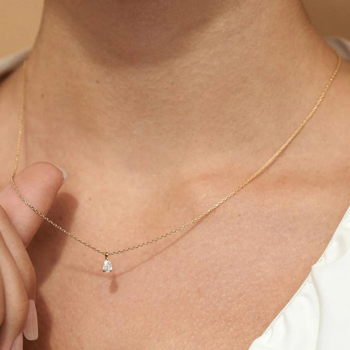 Gold necklace with a small pendant on a person's neck against a beige background