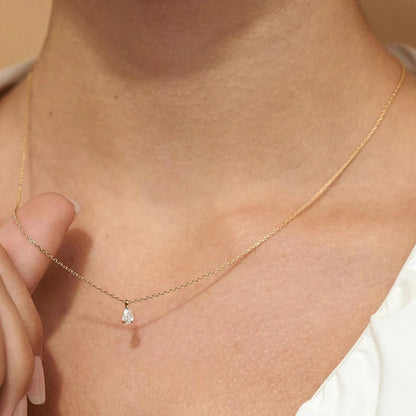 Gold necklace with a small pendant on a person's neck against a beige background