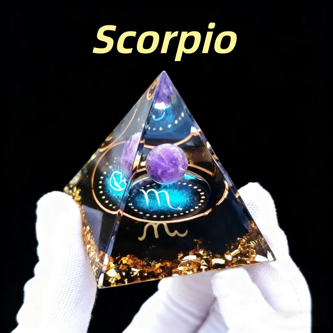 Pyramid-shaped decorative item with 'Scorpio' text and astrological symbol, held by a gloved hand against a black background.