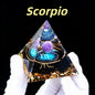 Pyramid-shaped decorative item with 'Scorpio' text and astrological symbol, held by a gloved hand against a black background.