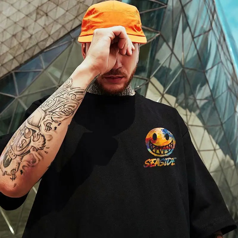 Person wearing a black t-shirt with a colorful logo and an orange cap, standing in front of a modern architectural background.