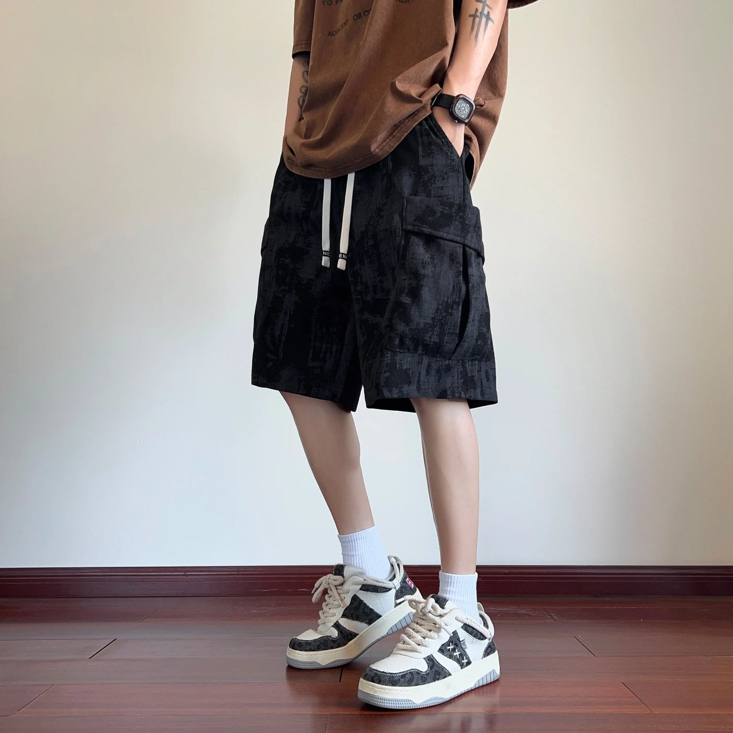 Person wearing black cargo shorts, a brown shirt, and white sneakers on a plain background