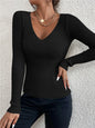 Person wearing a black ribbed long-sleeve top against a light gray wall.