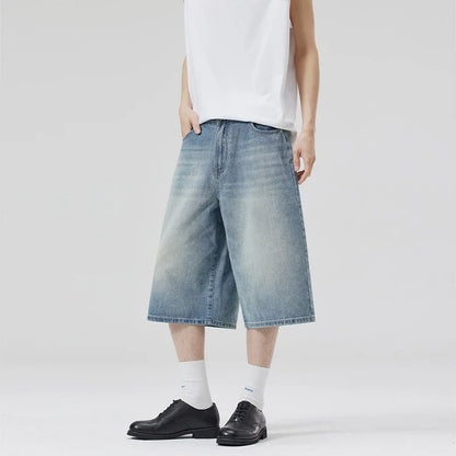 Person wearing light blue denim shorts, white shirt, black shoes, and white socks on a plain background