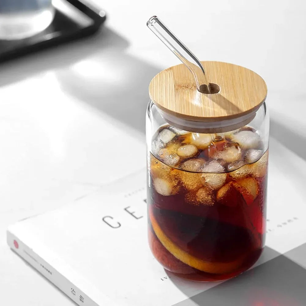 Glass drink container with wooden lid and straw on a light surface