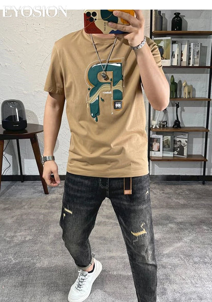 Person wearing a beige t-shirt with a graphic design and dark jeans in an indoor setting.