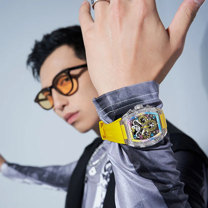 Person wearing a watch with a yellow strap and intricate face, against a neutral background