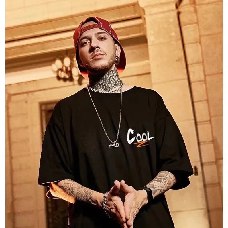 Man wearing a black oversized shirt with 'COOL' printed on it, standing in front of a building.