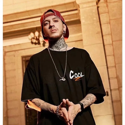 Man wearing a black oversized shirt with 'COOL' printed on it, standing in front of a building.