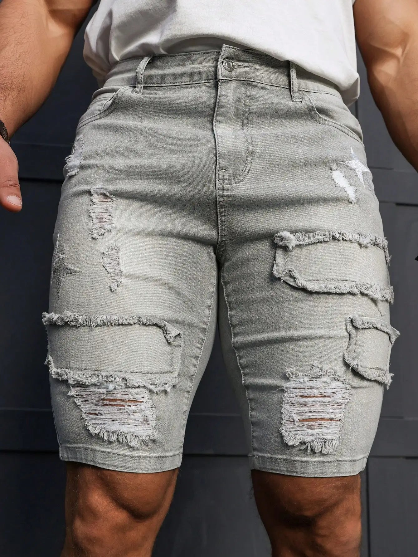 Ripped light gray denim shorts worn by a person against a dark background