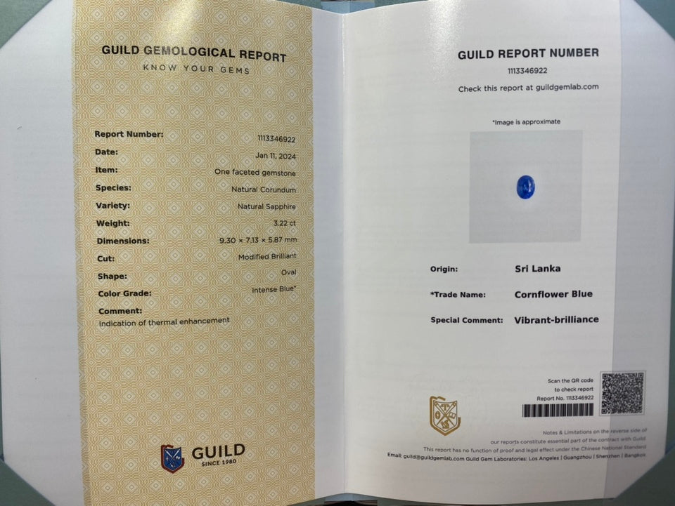 An open Guild gemological certificate report booklet showing both sides of the document. The left page has a gold patterned border and text detailing a natural corundum gemstone, while the right page contains report number details, origin, and a small blue gemstone color swatch.