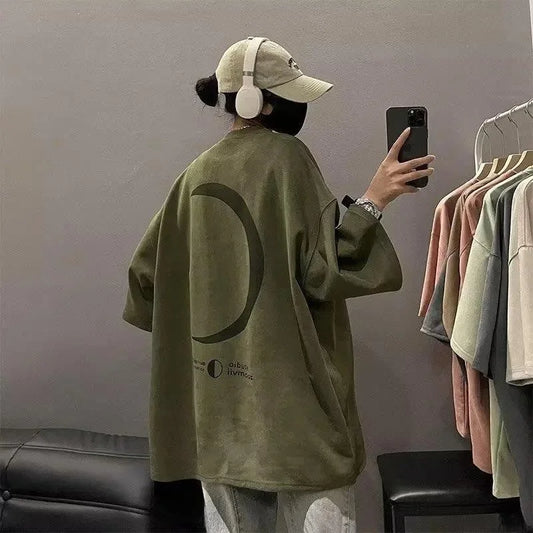 Person wearing a green oversized shirt with a large circle design, taking a mirror selfie.