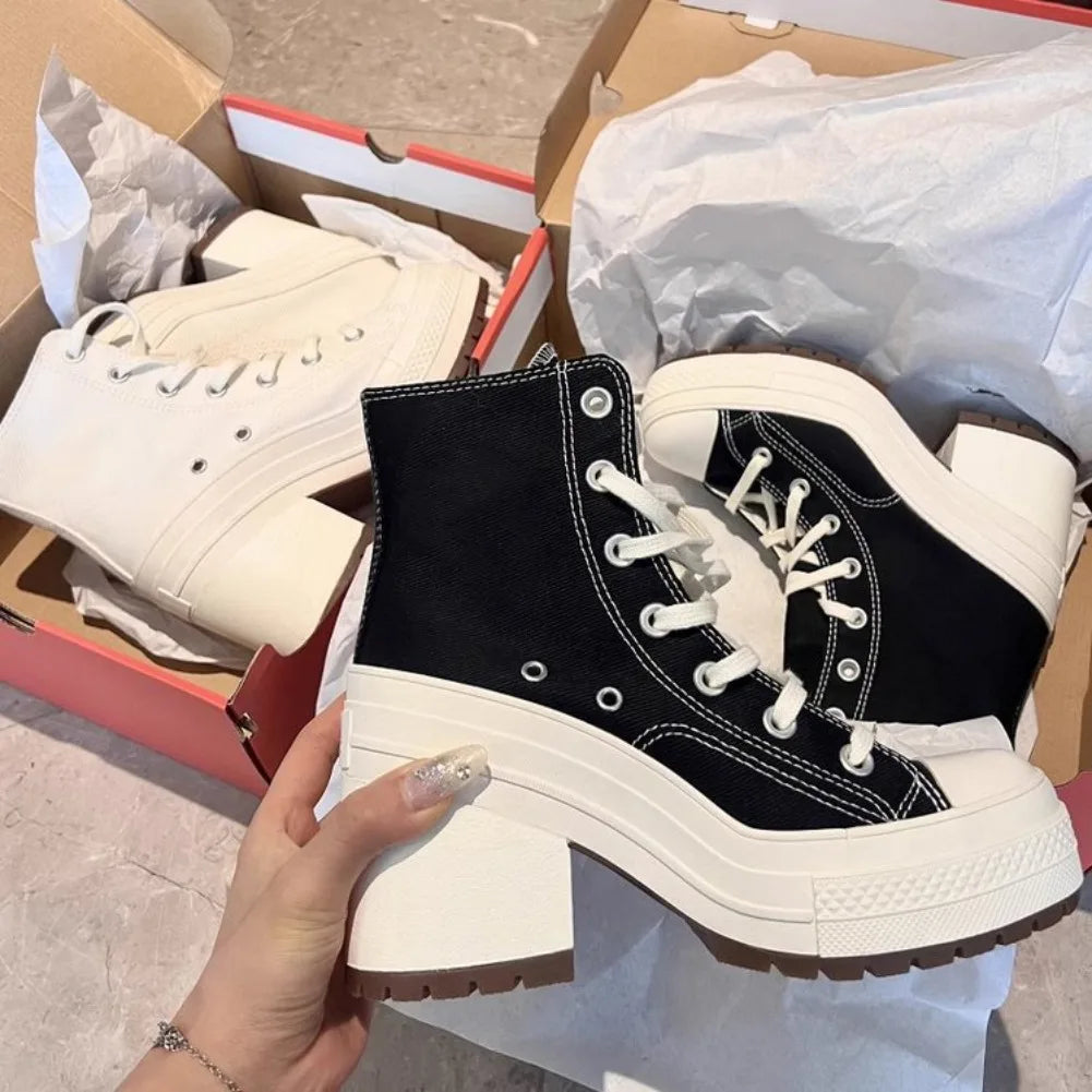 Black and white boots held by a hand with a cardboard box and white shoes in the background.