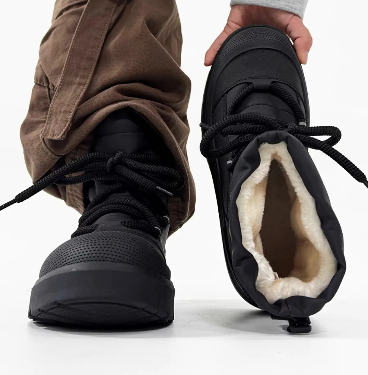Black winter boots with fur lining worn by a person on a white background