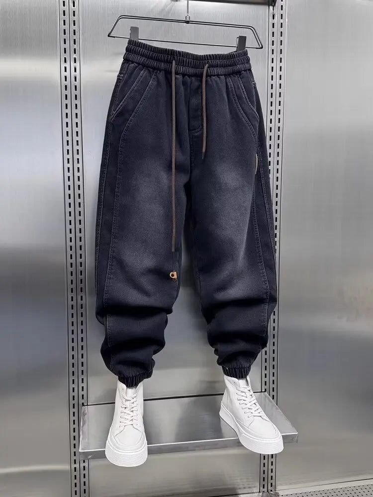 Black jogger pants on a hanger with white sneakers below against a metallic background