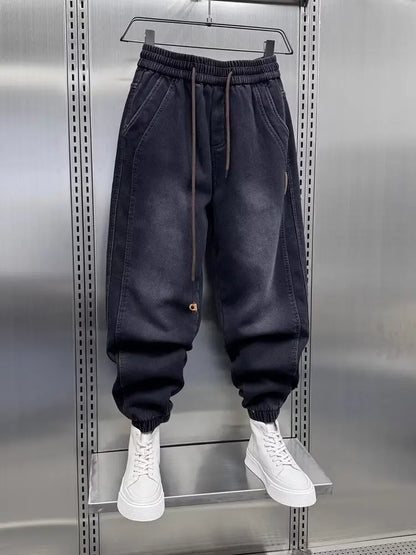 Black jogger pants on a hanger with white sneakers below against a metallic background