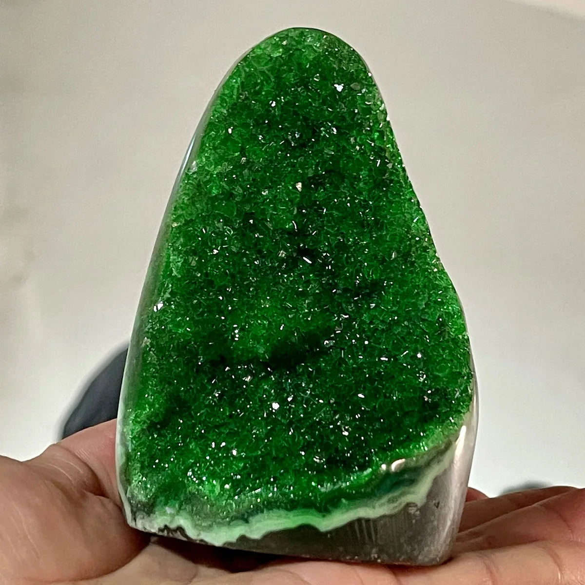 Green crystal held in a hand against a neutral background