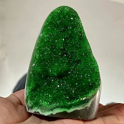 Green crystal held in a hand against a neutral background