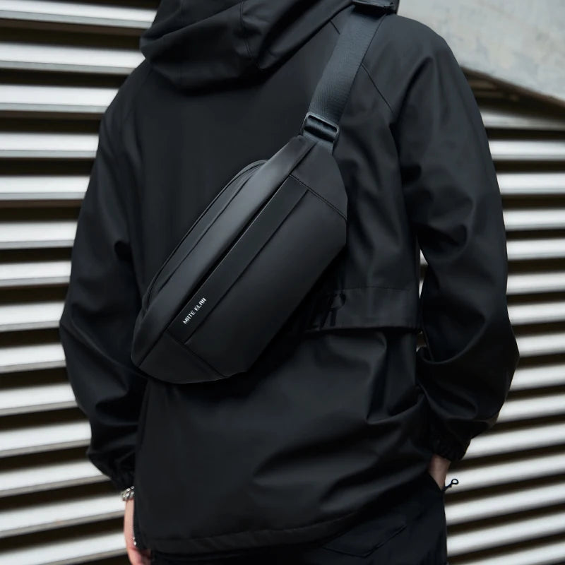 Person wearing a black jacket with a matching black waist bag against a metallic background
