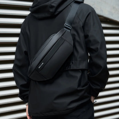 Person wearing a black jacket with a matching black waist bag against a metallic background